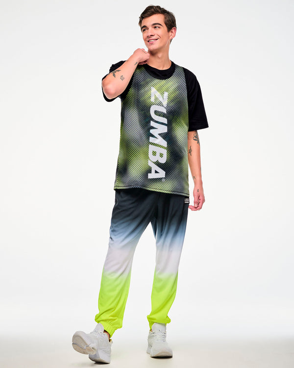 Full view of a male model wearing a black top with a yellow halftone dot-print panel, ombre joggers, and white sneakers.