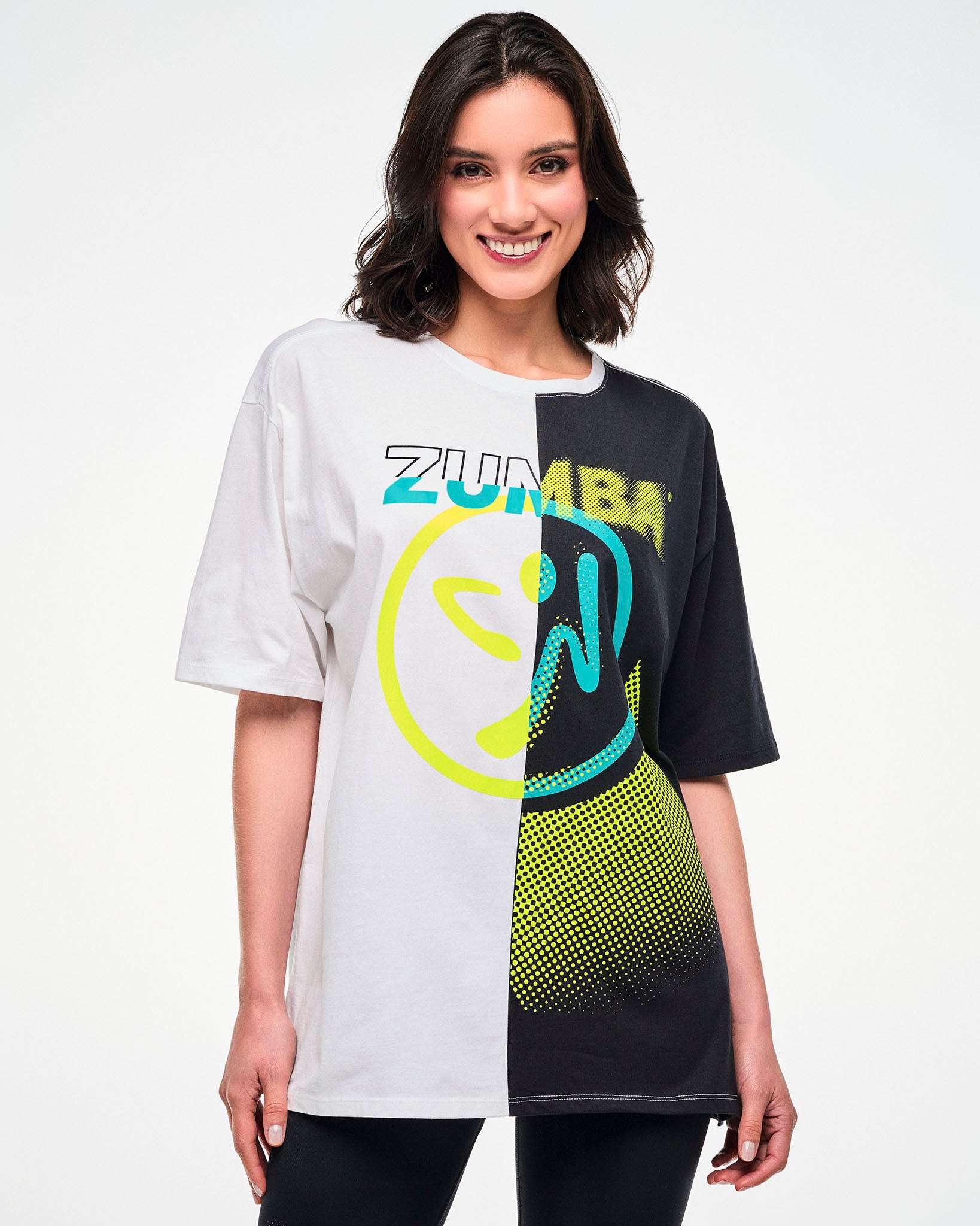 Female model wearing a black and white colorblock oversized T-shirt with a yellow and aqua "ZUMBA" Zumbito graphic.