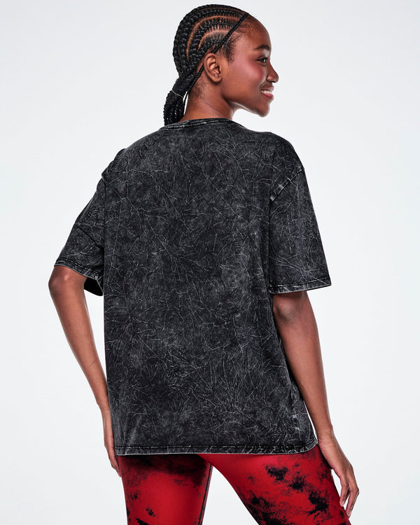 Female model wearing a dark gray acid-wash tee, shown from the back against a plain white studio background.