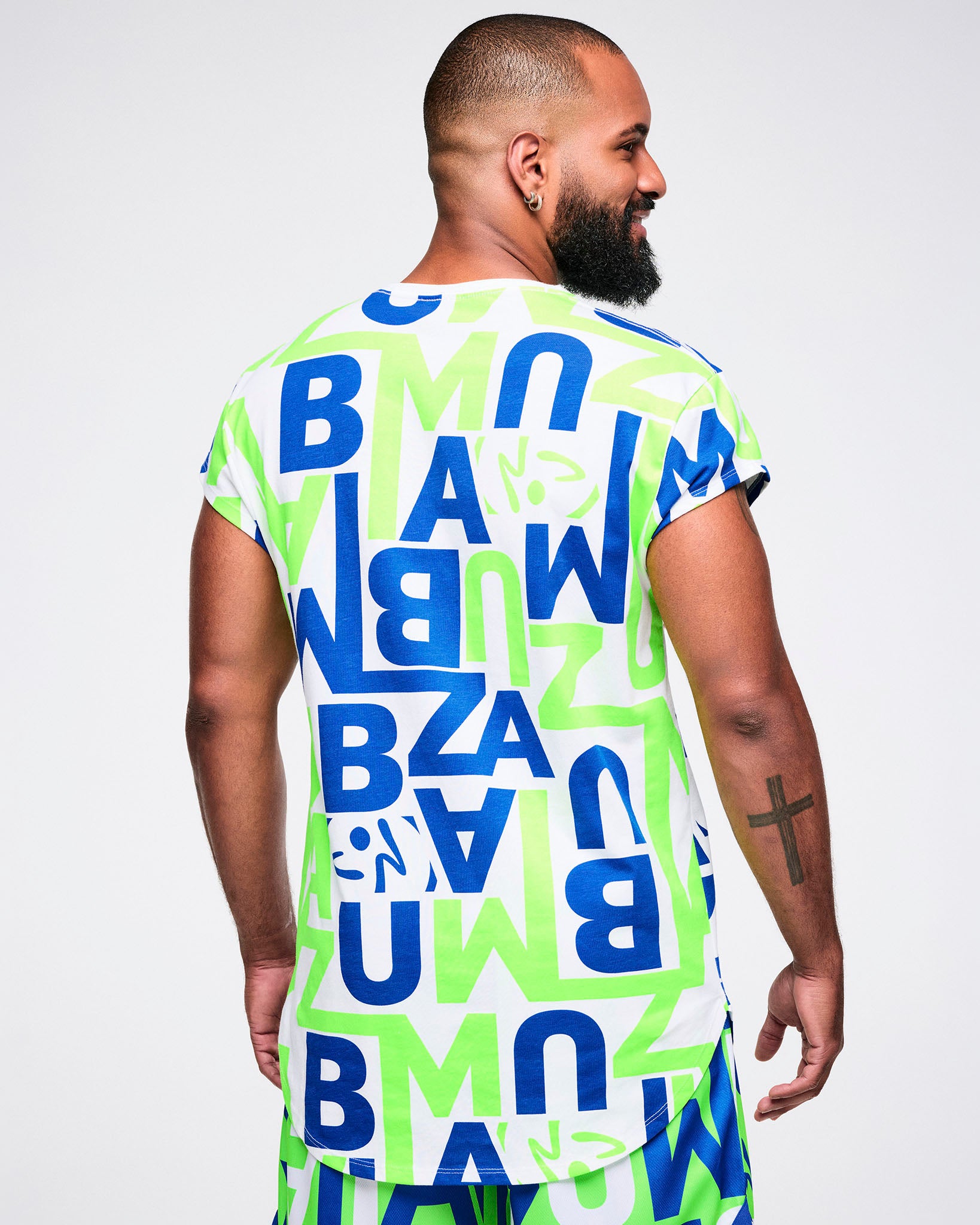 Back view of a male model wearing a colorful t-shirt with "ZUMBA" letter patterns on a plain background.
