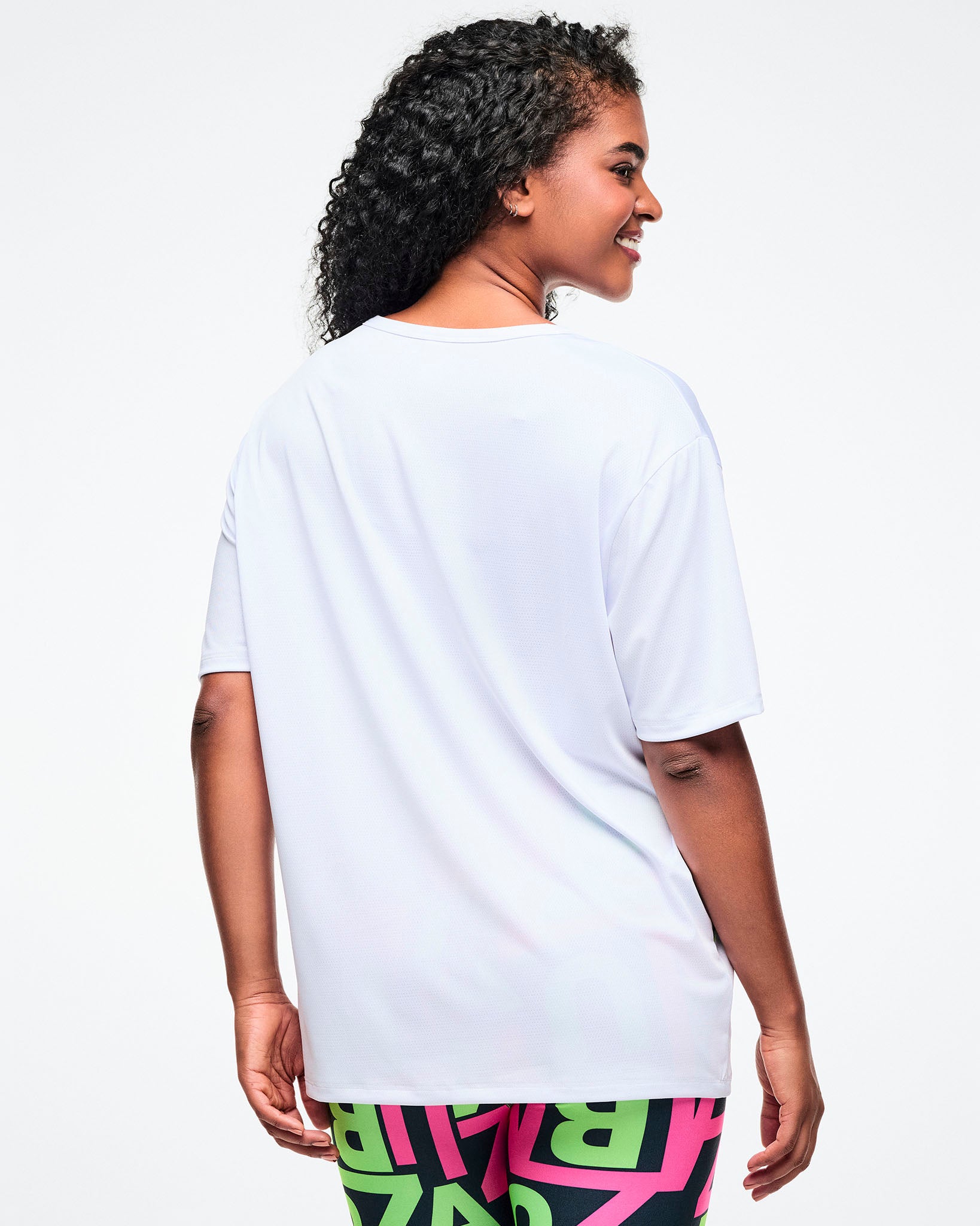 Back view of a female model in a white Zumba top against a white background.