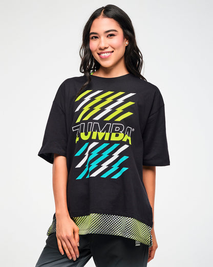 Female model wearing a black oversized T-shirt with black and yellow "ZUMBA" text outlined in white in the middle, yellow and aqua lightning graphics, and a mesh dot-print hem.
