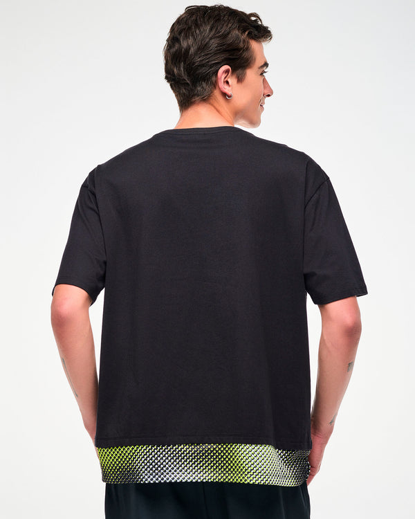 Male model wearing a black oversized T-shirt with a yellow, black, and white mesh dot-print hem, shown from the back.