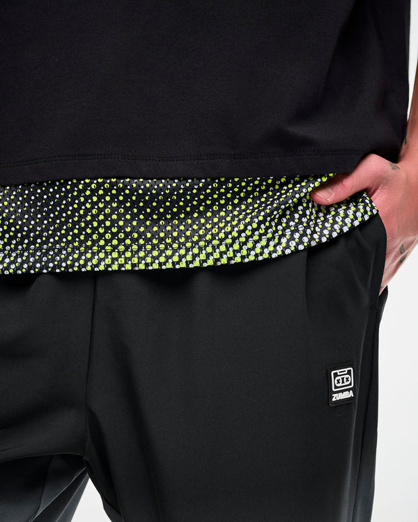 Close-up of a black mesh dot-print hem on an oversized T-shirt, paired with black track pants featuring a cassette tag.