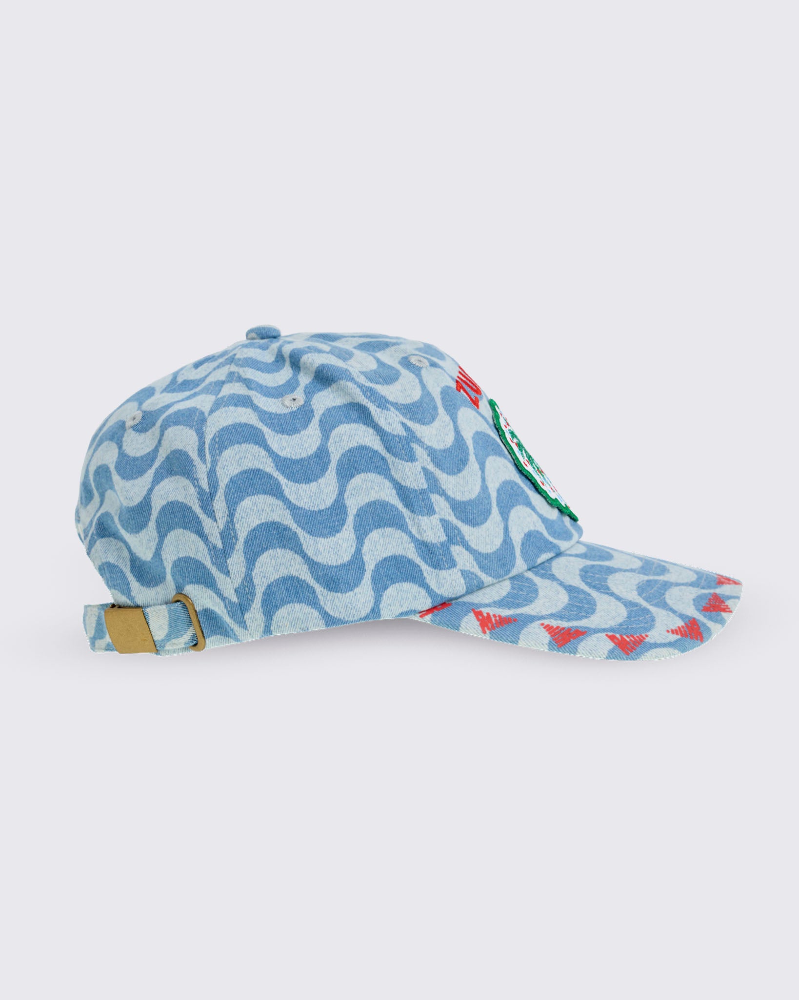 Light blue wavy-print baseball cap with curved brim, embroidered “ZUMBA” text and palm-tree patch on the front, and an adjustable back strap with metal buckle, shown in side view on a white background.