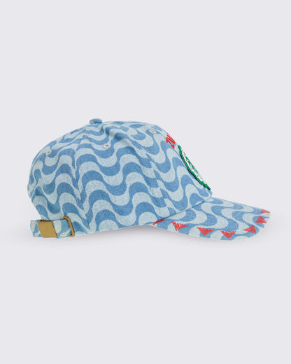 Light blue wavy-print baseball cap with curved brim, embroidered “ZUMBA” text and palm-tree patch on the front, and an adjustable back strap with metal buckle, shown in side view on a white background.