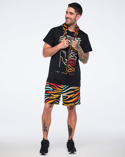 Multicolor Zumba square bandana worn around the neck on a male model. He wears a black graphic Zumba T-shirt, multicolor zebra-print shorts, and black sneakers in a full-body studio pose.