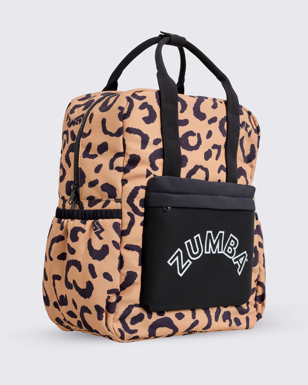 Leopard-print Zumba backpack shown at an angled front view from the opposite side, featuring black top handles, a black front pouch with white ZUMBA logo, side pockets, and a structured zip-top silhouette against a light gray background.