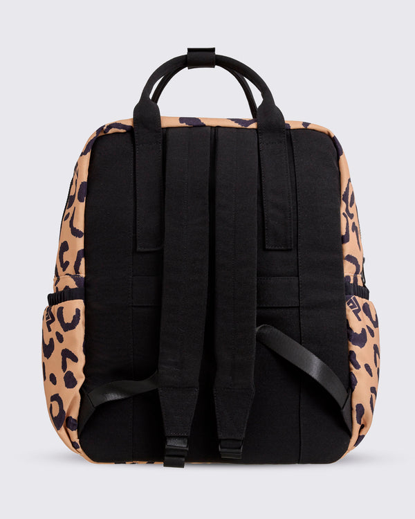 Back view of the leopard-print Zumba backpack with black padded shoulder straps, black back panel, top carry handles, and leopard-print sides with elastic side pockets against a light gray background.