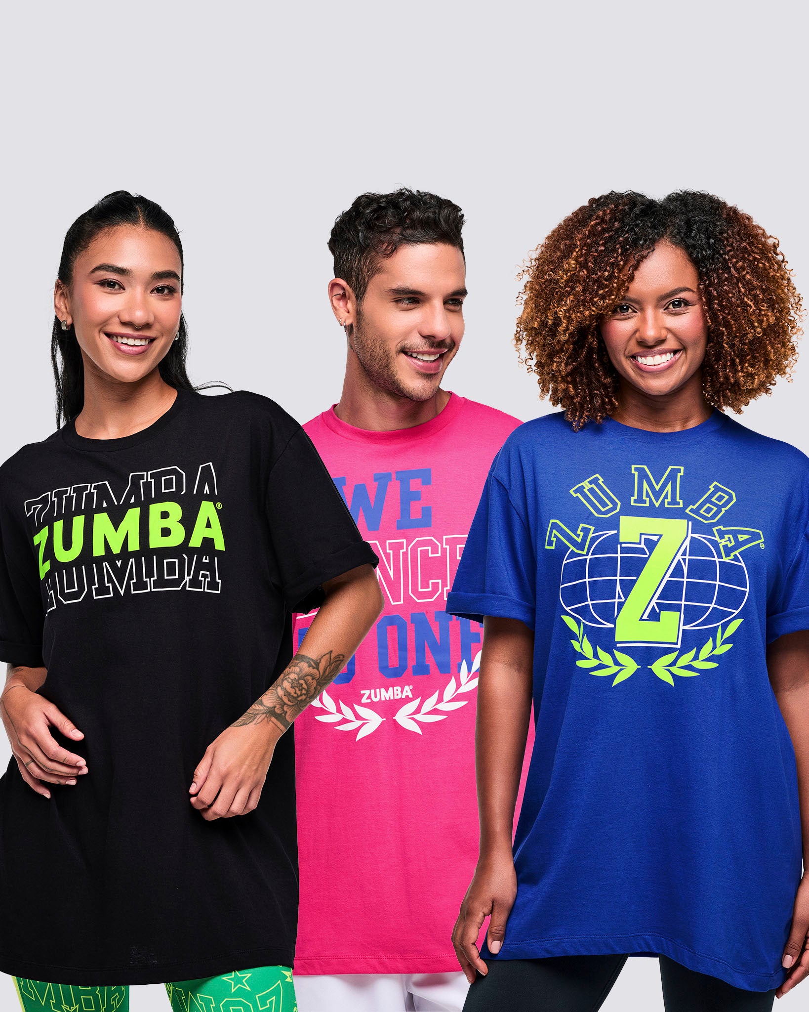 Three models—two female, one male—wearing vibrant Zumba T-shirts on a white background.