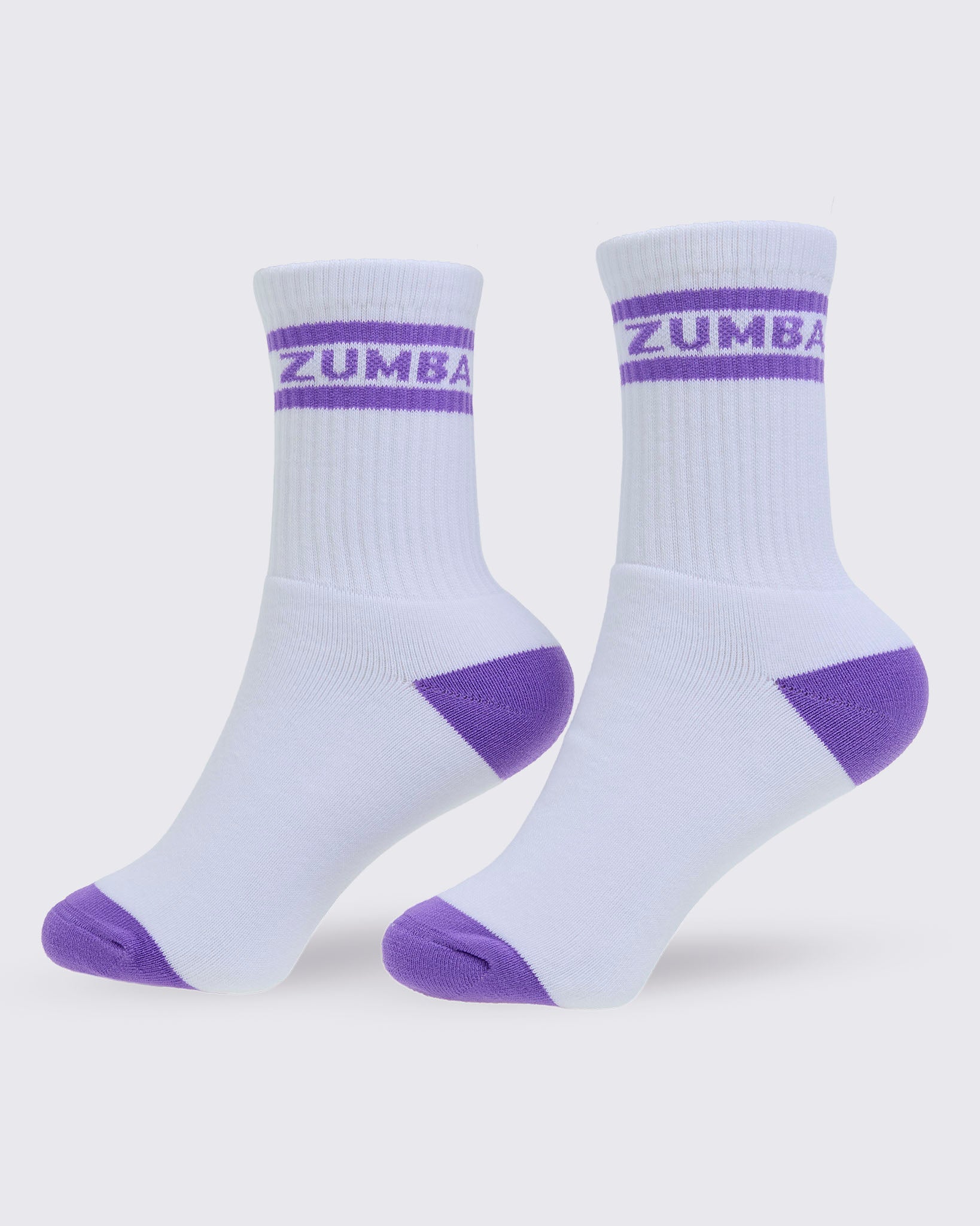 A pair of white crew socks with purple toe and heel accents, featuring a purple double stripe and 'ZUMBA' text on the ribbed cuff, set against a light gray background.