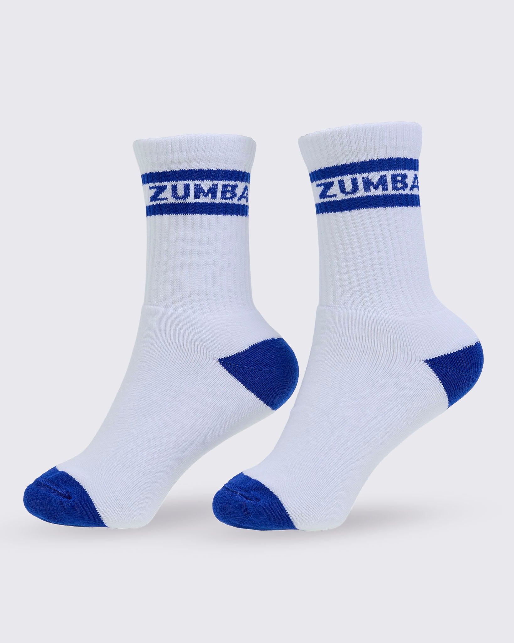 A pair of white crew socks with blue toe, heel, and sole accents, featuring the brand name 'ZUMBA' printed in white on a blue stripe at the ribbed cuff, set against a light gray background.