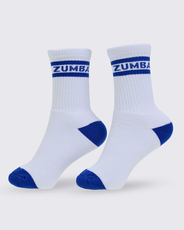 A pair of white crew socks with blue toe, heel, and sole accents, featuring the brand name 'ZUMBA' printed in white on a blue stripe at the ribbed cuff, set against a light gray background.