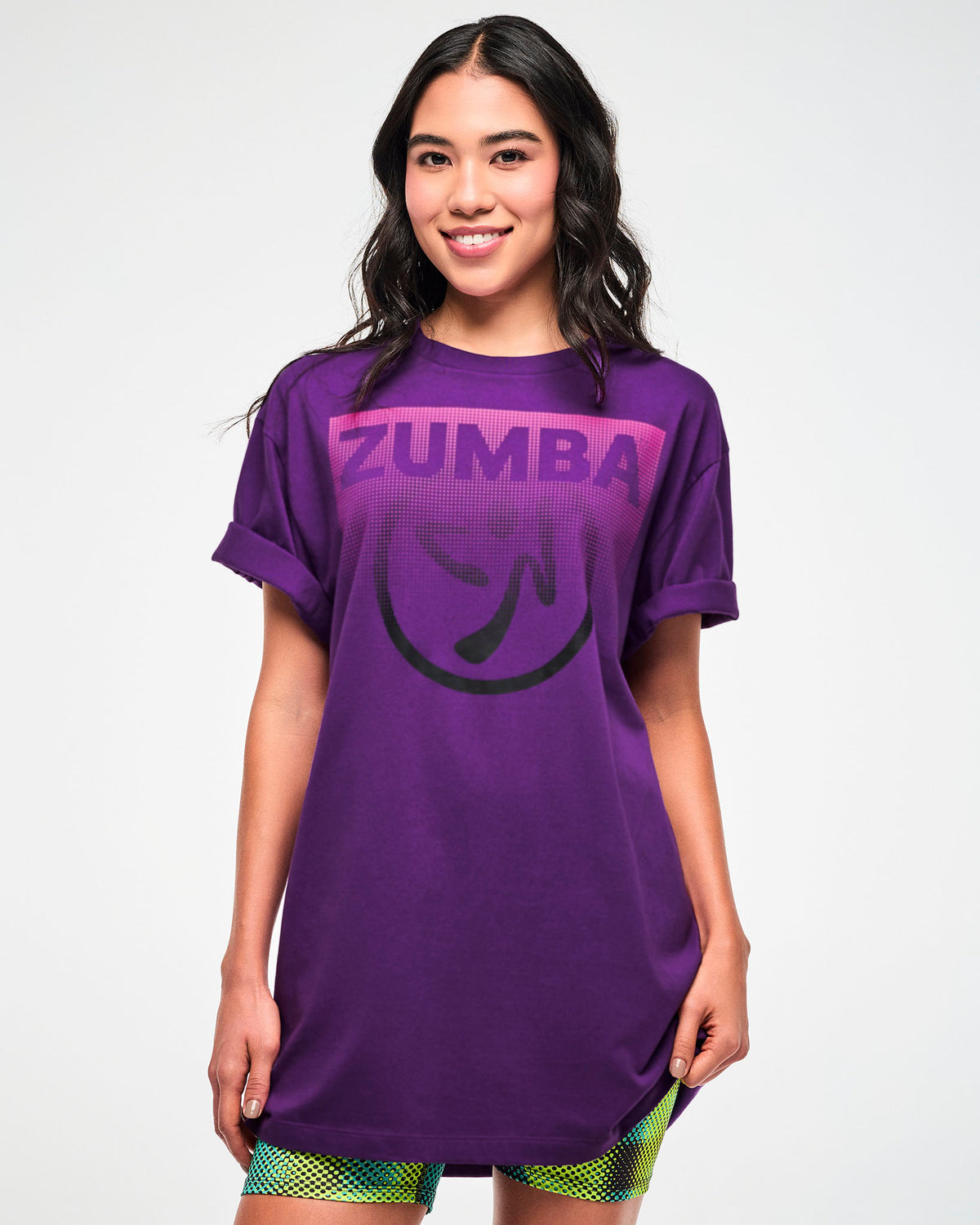 Female model wearing a purple T-shirt with a pink "ZUMBA" logo and black Zumbito graphic.