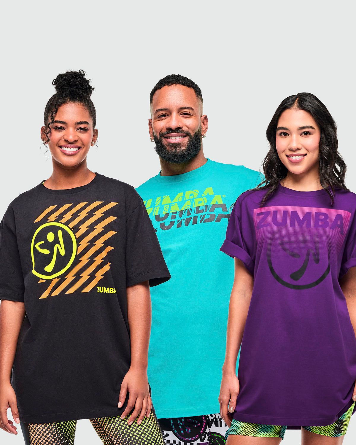 Three models wearing T-shirts in black (female), aqua (male), and purple, (female), each with a different "ZUMBA" graphic print.