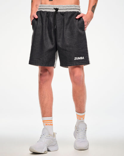 Male model wearing black and grey colorblock shorts with white "ZUMBA" text on the left leg, paired with orange-striped socks and white shoes.