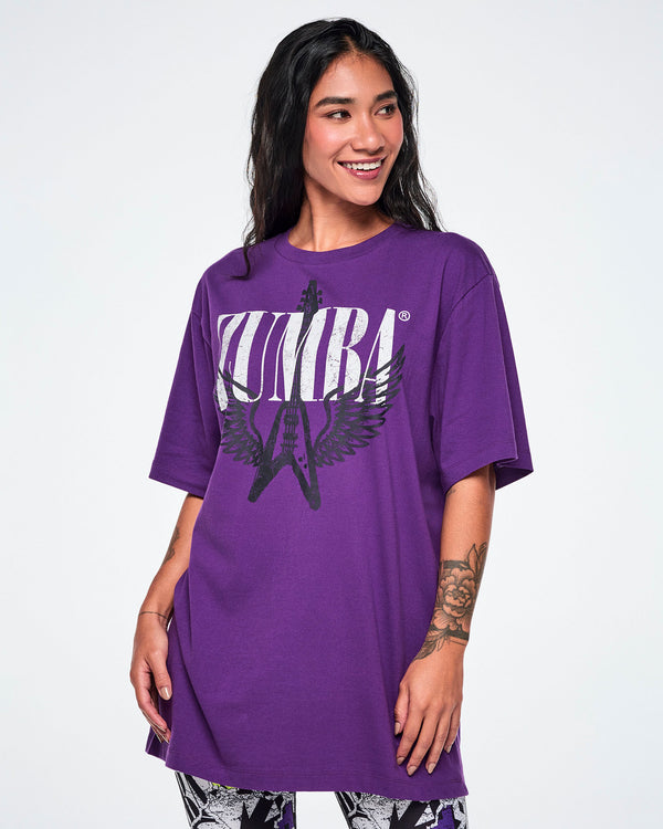 A female model wearing an oversized purple t-shirt with large white ZUMBA text and black winged guitar graphic on the front, set against a plain light gray background.