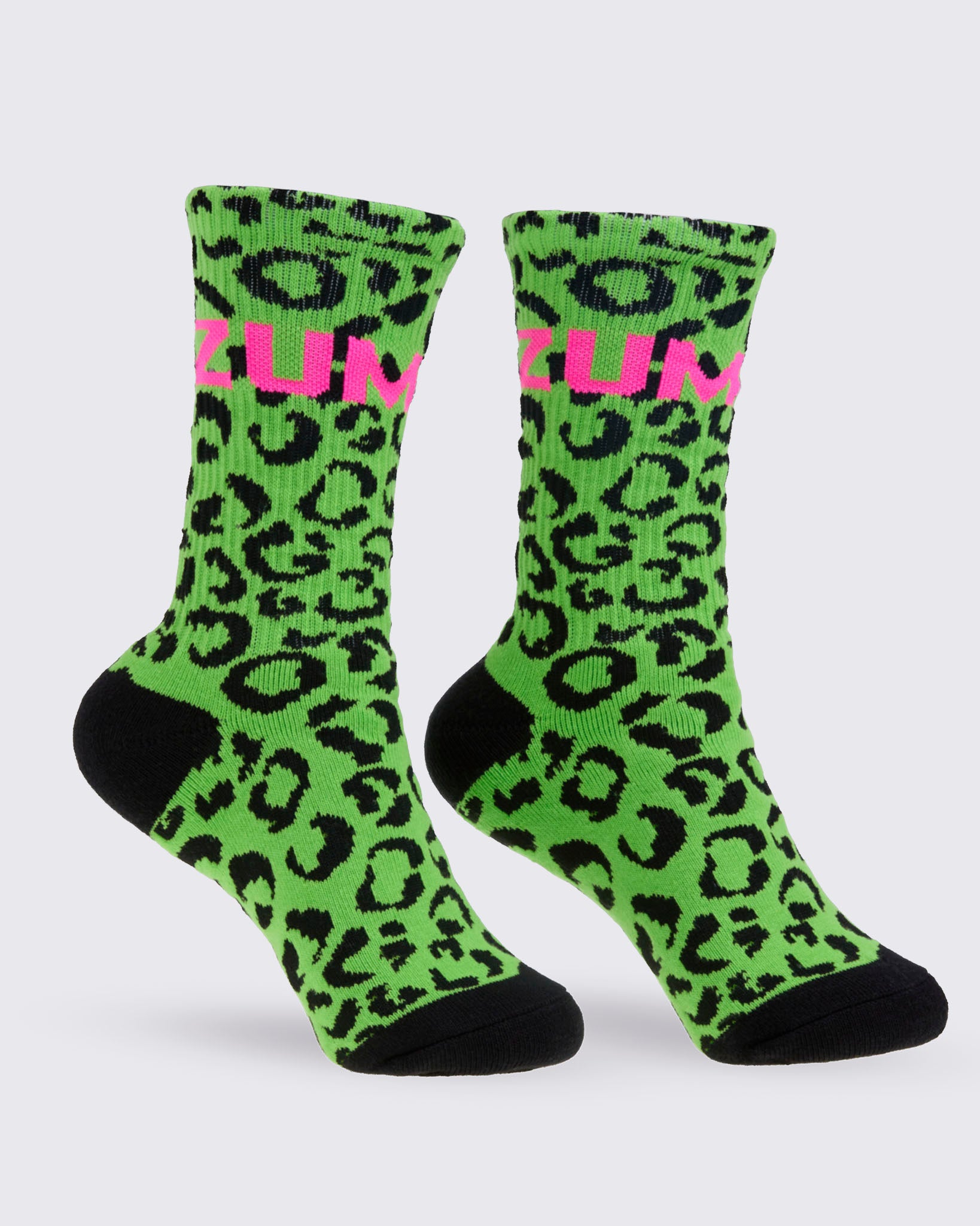 A pair of high socks featuring a bright green and black leopard print pattern, with a pink 'ZUMBA' text on the top and solid black toes and heels, shown against a white background.