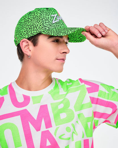 Male model from the side wearing a green cap with leopard print and a colorful shirt with letters.