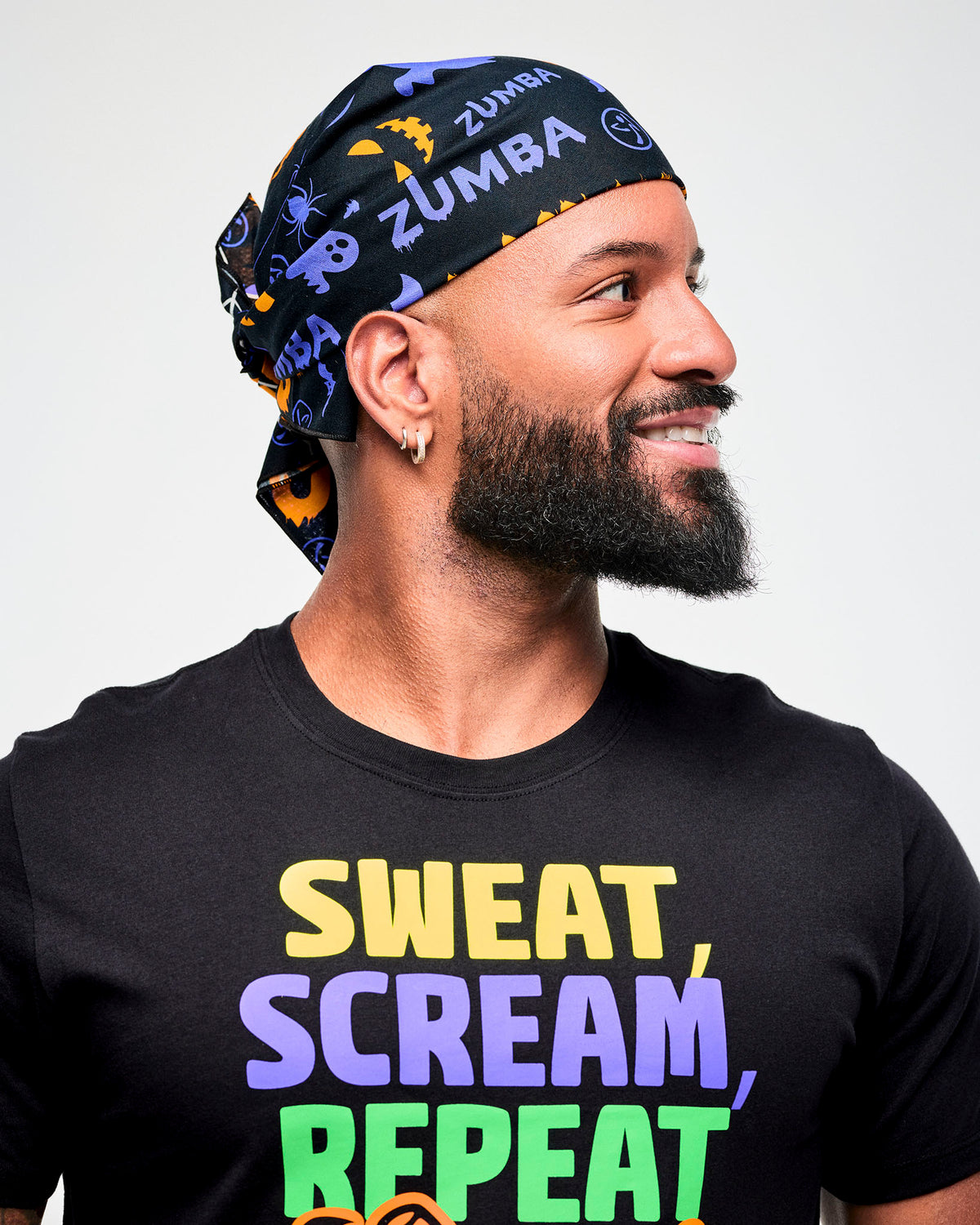 Male model wearing a black and purple Halloween-print bandana as a headwrap with a black "Sweat, Scream, Repeat" Halloween tee.