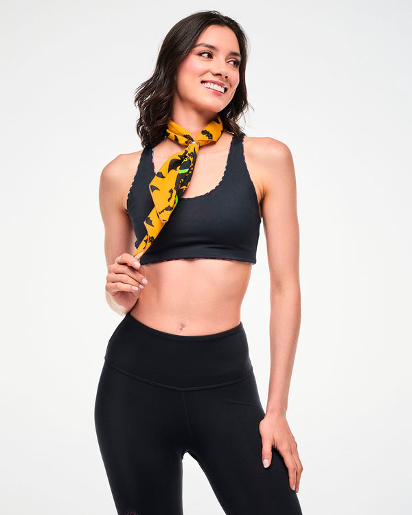 Female model wearing an orange bat-print bandana tied around the neck, paired with a black reversible bra top and leggings.