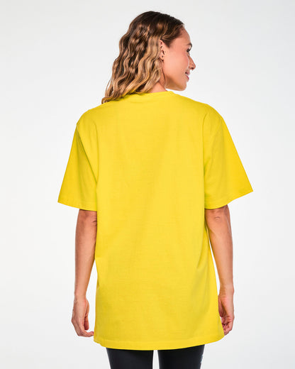 Back view of a female model in the yellow 'FRONT ROW DIVA ENERGY' Smurfette tee, showing a plain back and a relaxed, long fit.