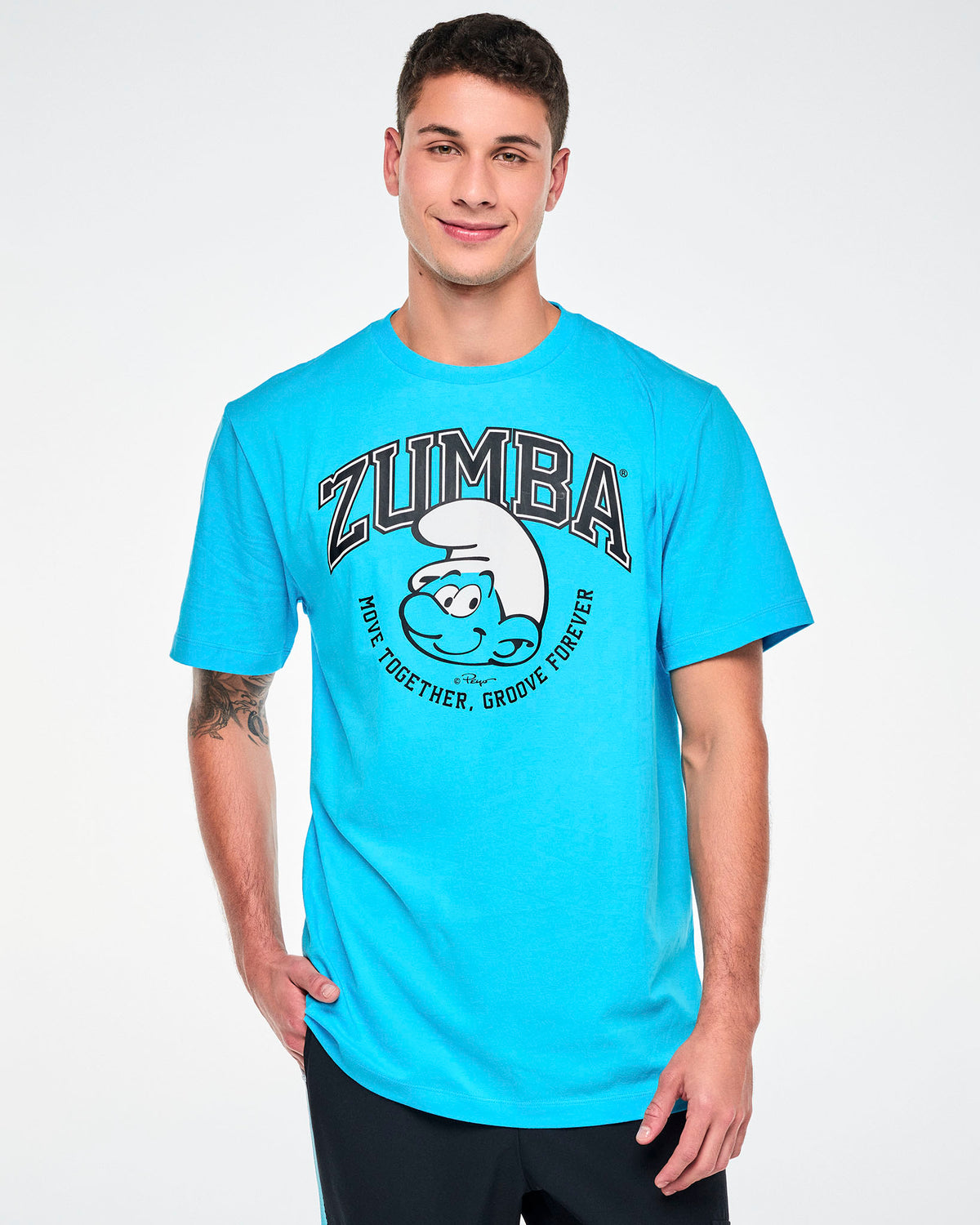 Male model in a blue crew neck tee with arched black varsity 'ZUMBA' text over a large smiling Smurf face in a white hat, framed by curved 'MOVE TOGETHER, GROOVE FOREVER' text. Paired with black pants.