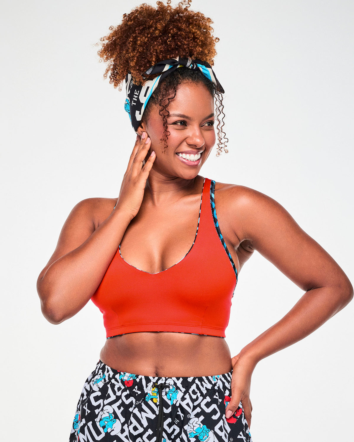 Female model wearing the black and white Smurfs text bandana tied around her hair with a knot on top, paired with a red bra and Smurfs print cargo pants.