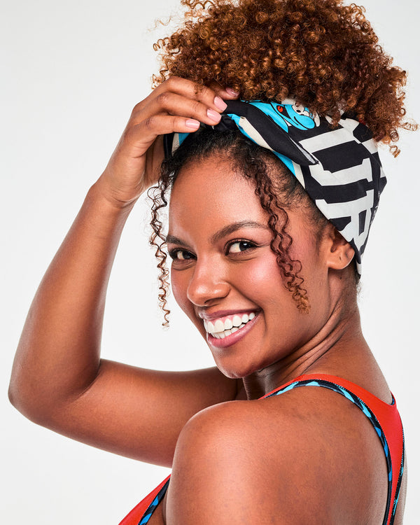 Close-up of a female model adjusting the bandana tied around her hair, showing the bold white lettering and a blue Smurf on the black fabric.