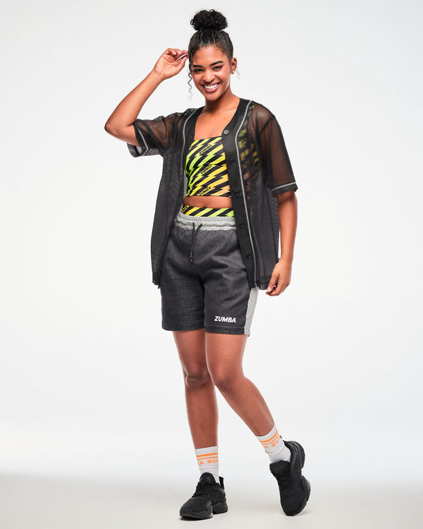 Female model wearing black and grey shorts, black shoes and paired with a sheer black button-up top and printed crop top.