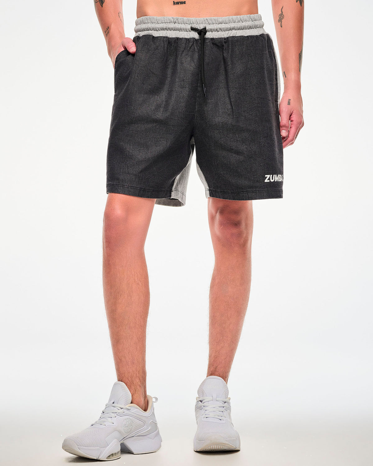 Close-up of a male model wearing black and grey shorts with a cinched drawstring waist and white "ZUMBA" text.