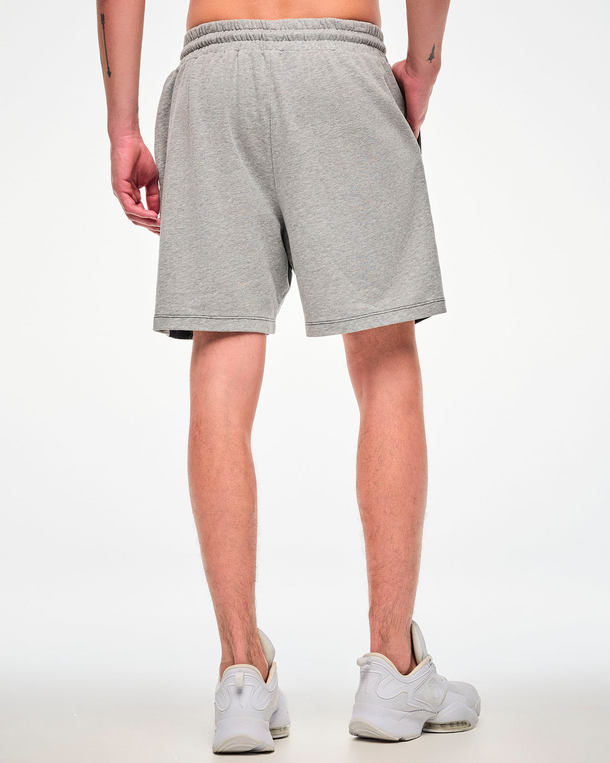 Shown from the back, male model wearing grey shorts paired with white sneakers.