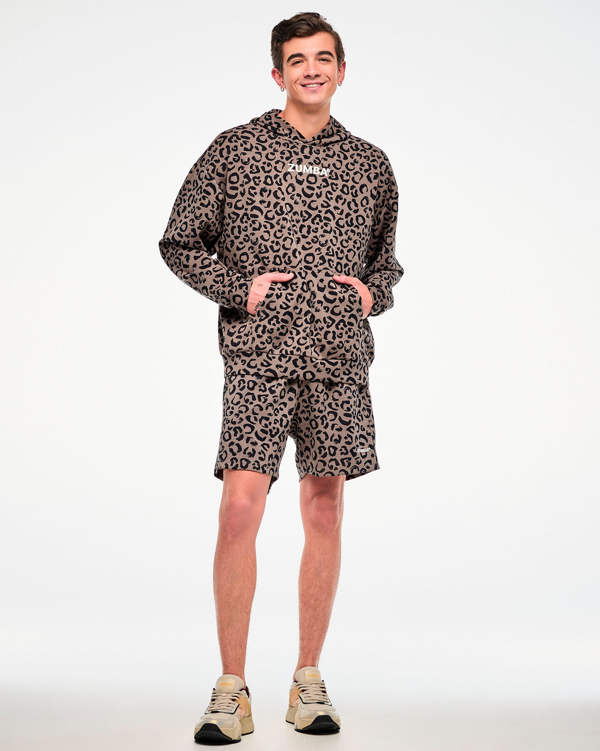 Full view of a male model in the leopard print easy shorts with a matching brown leopard print hooded pullover sweatshirt and beige shoes.