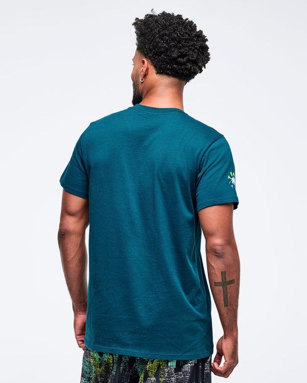 Back view of the teal short-sleeve crewneck T-shirt with a clean, solid back, modeled by a male wearing patterned shorts on a white studio background.