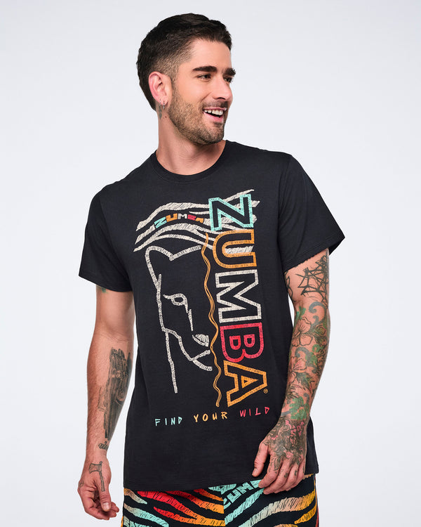 Black short-sleeve Zumba graphic T-shirt with a crew neckline and relaxed fit, featuring a multicolor front design with a lion face outline, vertical “ZUMBA” text, and “Find Your Wild” lettering. Male model wears the T-shirt with multicolor print shorts.
