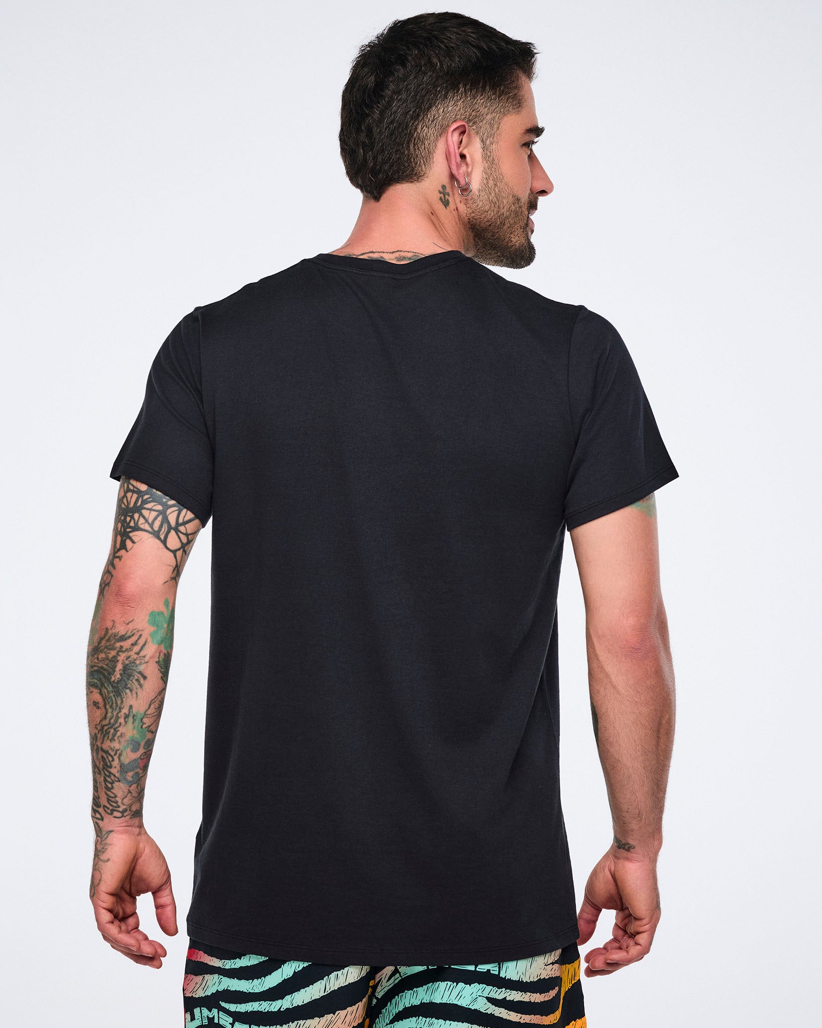 Back view of a black short-sleeve T-shirt with a crew neckline, straight hem, and relaxed fit. Male model wears the T-shirt with multicolor striped print pants.