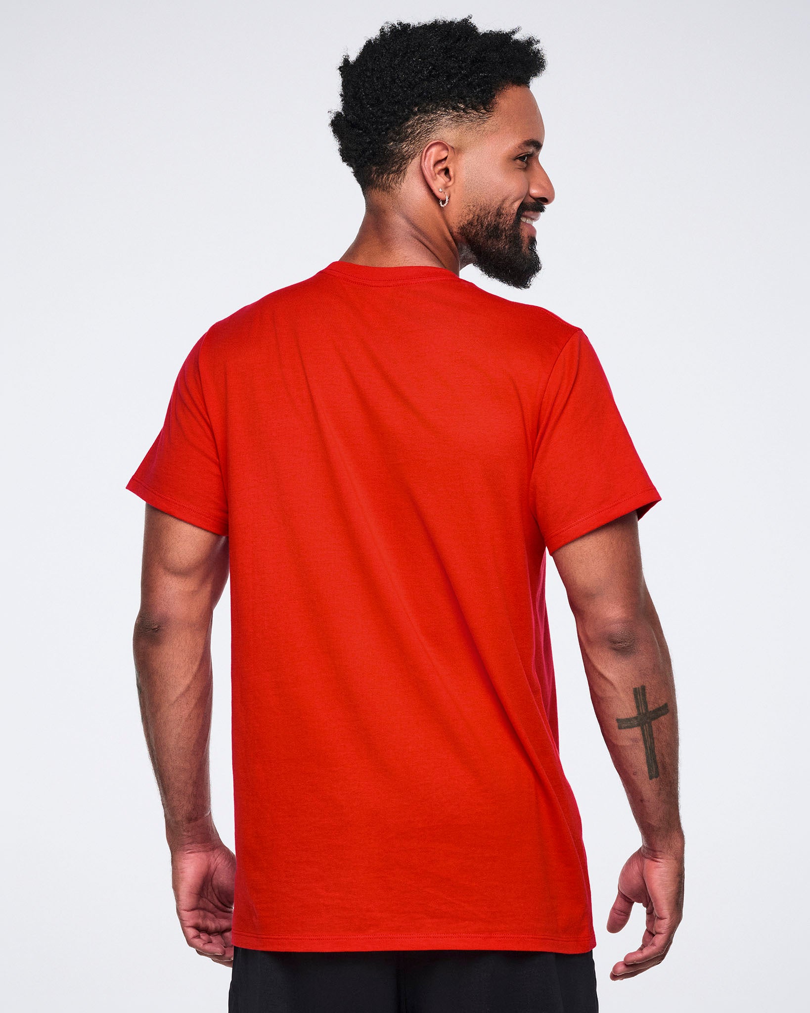 Male model wearing a red crewneck T-shirt shown from the back with short sleeves and a relaxed fit, paired with black athletic pants.