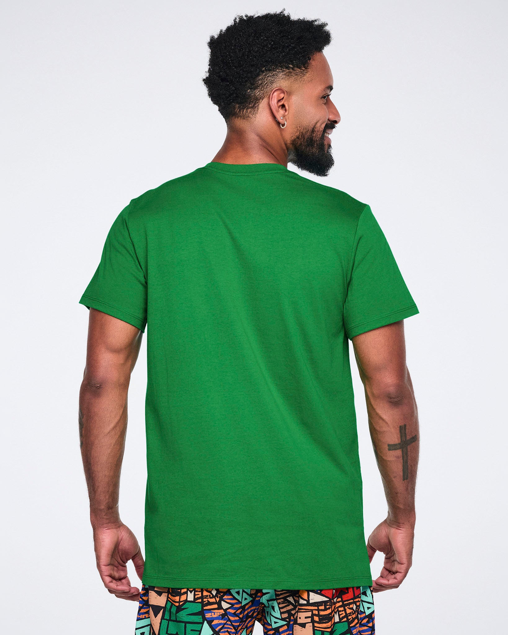 Back view of a green short-sleeve graphic T-shirt with a crew neckline, straight hem, and relaxed fit. Male model wears the T-shirt with multicolor print pants.