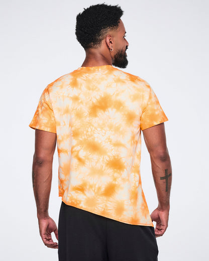 Male model wearing an oversized orange and white tie-dye T-shirt shown from the back with short sleeves, an asymmetric hem, and black wide-leg athletic pants.
