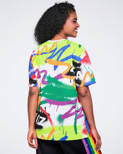 Back view of a female model wearing a colorful graphic t-shirt with abstract designs on a white background.