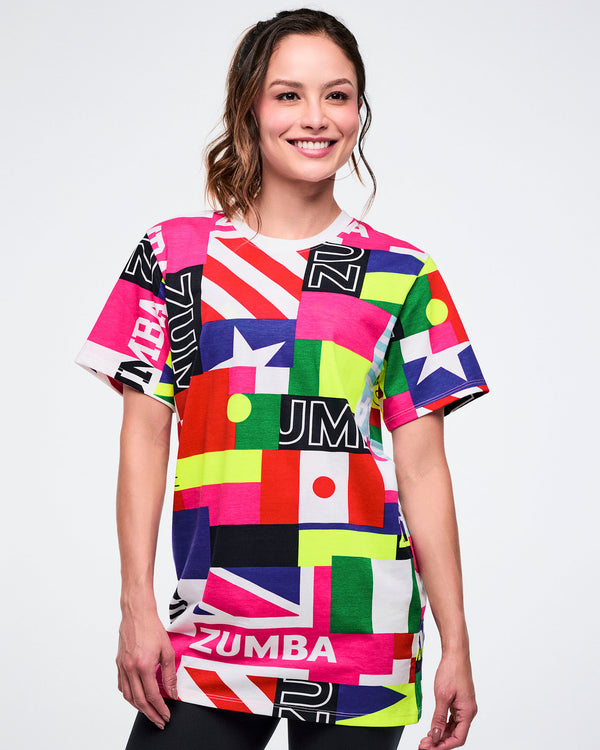 Female model wearing a colorful Zumba shirt with various flag patterns against a white background.