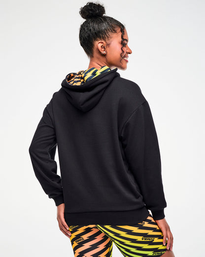 Shown from the back, female model wearing a black hoodie with an orange, yellow, and green ombre lightning bolt-print hood lining, paired with matching biker shorts.