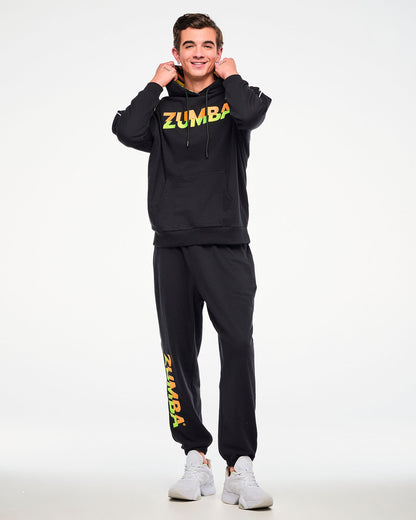 Male model wearing a black hoodie and matching joggers with a gradient "ZUMBA" logo, paired with white sneakers.