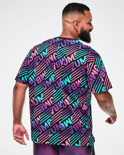 Shown from the back, male model wearing a black tee with a colorful pink, aqua, and  purple diagonal striped "ZUMBA" broken patterned print.