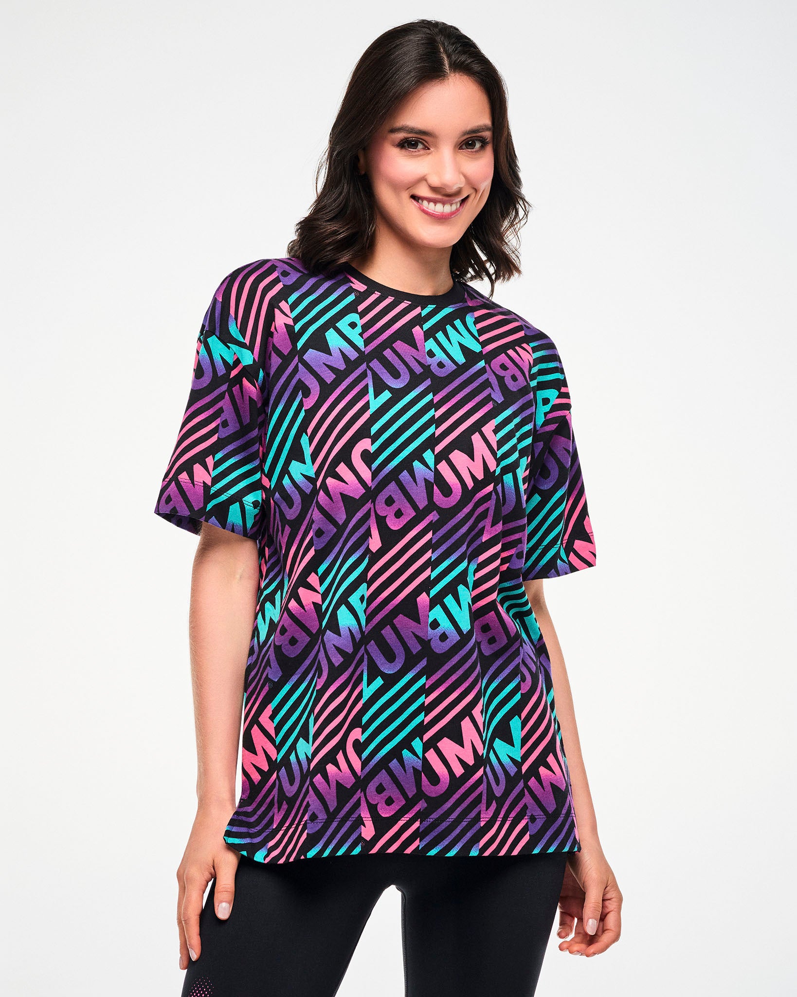 Female model wearing a black tee with a colorful pink, aqua, and purple diagonal striped "ZUMBA" broken patterned print.