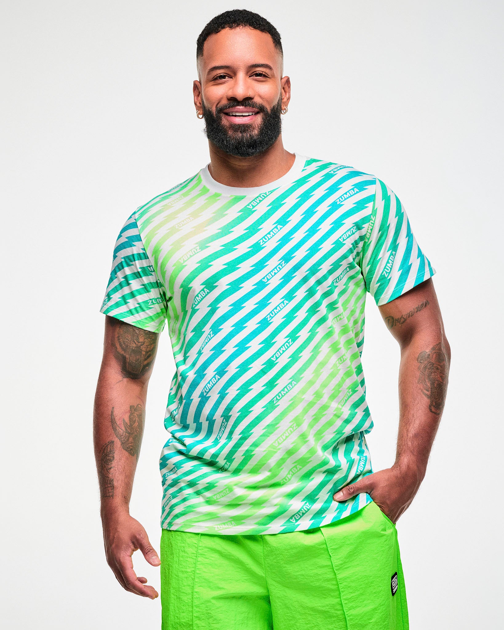 Male model wearing a green and aqua lightning bolt-striped tee with "ZUMBA" text, paired with lime green shorts.