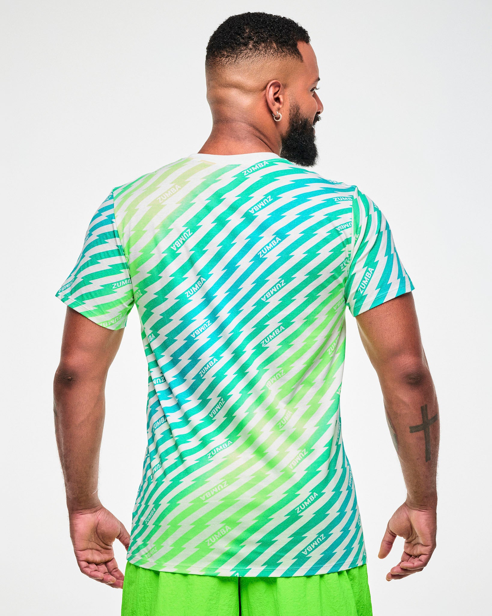 Male model wearing a green and aqua lightning bolt-striped tee with "ZUMBA" text, paired with lime green pants, viewed from the back.