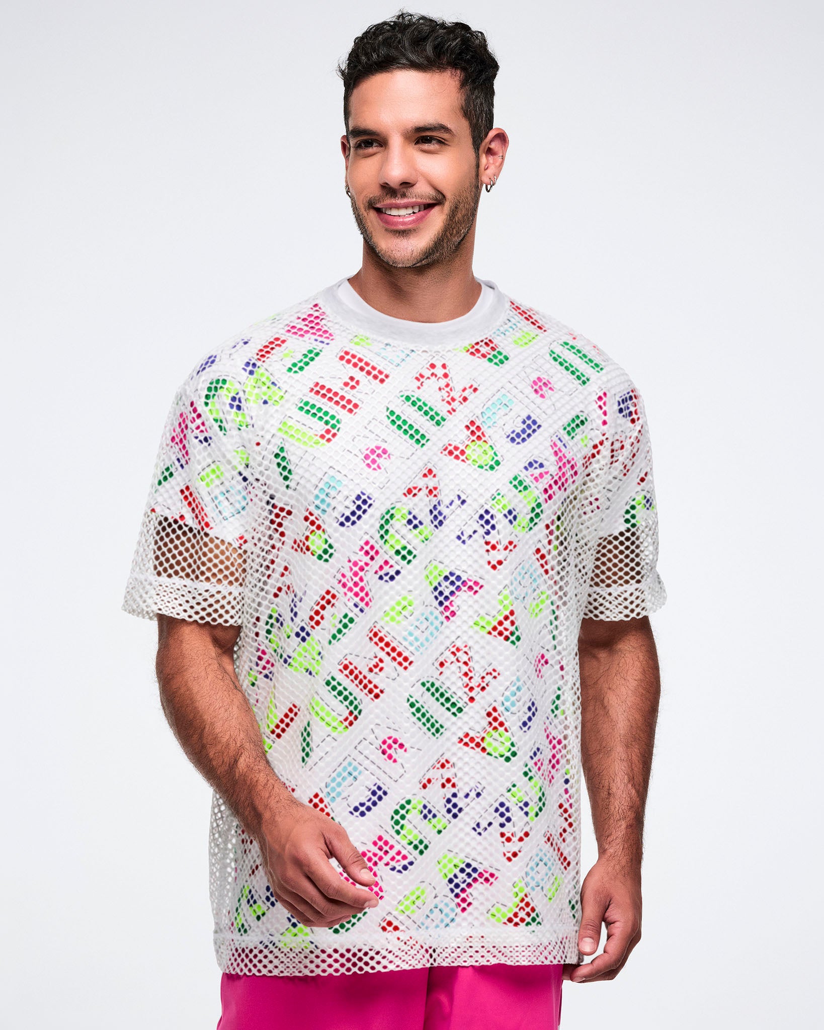 Male model wearing a patterned shirt layered with a white mesh top and paired with pink pants, set against a white background.
