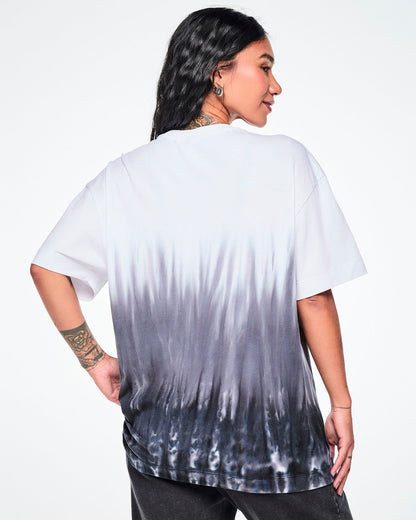 Back view of a female model wearing a white tee with a black-to-white tie-dye flame pattern at the bottom, paired with black pants.