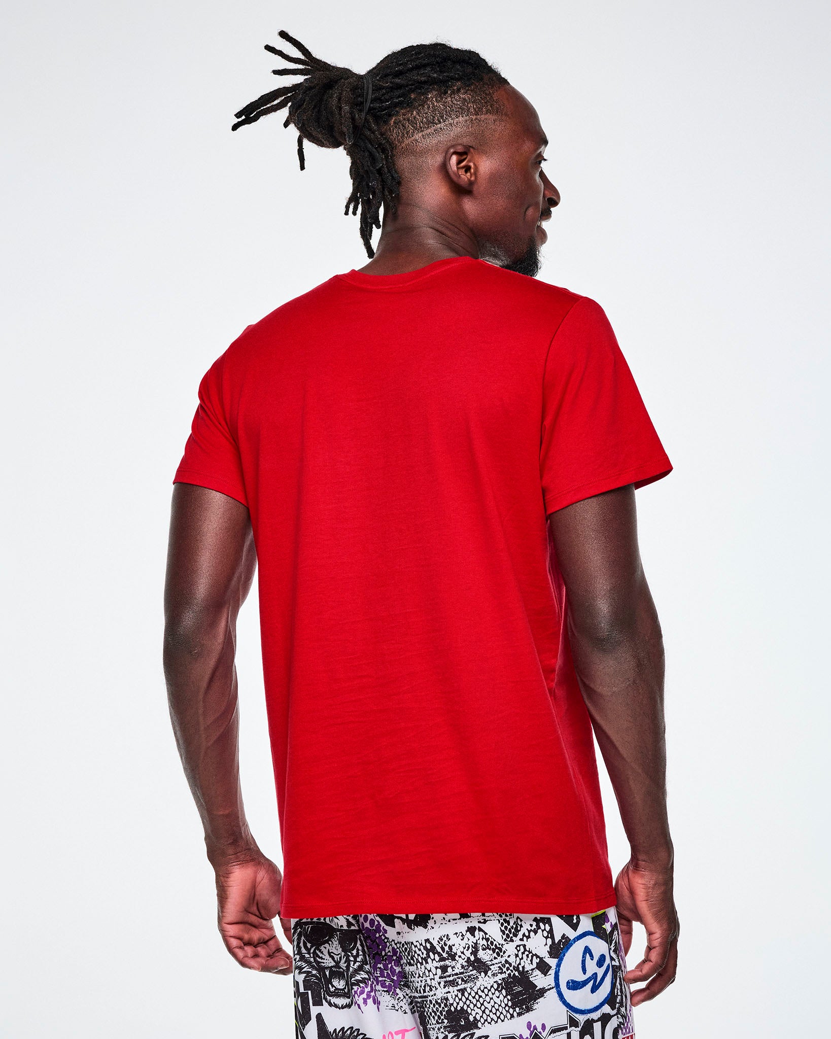 A male model wearing a red short-sleeve tee and multi-colored pants.